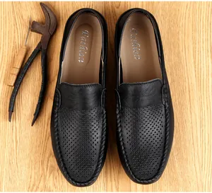Primer plano de mocasines de cuero negro perforado presentados sobre una superficie de madera.