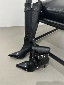 Close-up of black retro tall boots featuring silver studs and a sharp pointed toe design.