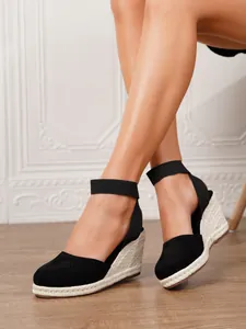 Vista detallada de alpargatas de cuña en ante negro con suelas de yute natural trenzado.