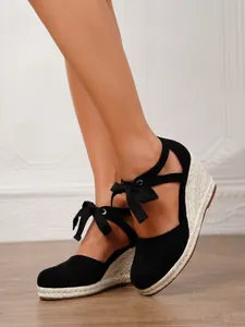 Detalle de sandalias de cuña negras con lazos al tobillo y suelas de esparto trenzado.