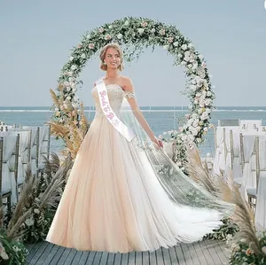 Elegant white satin Bride to Be sash with pink lettering shown on a model at a beach wedding