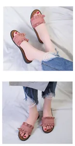 Detailed view of pink ruffled flat slide sandals worn with frayed denim jeans