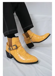 Close-up of yellow crocodile embossed Chelsea boots with decorative metal buckle and chain