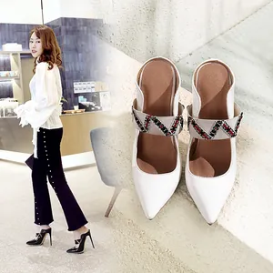 Detailed close-up of white pointed-toe high heel mules featuring embroidered elastic straps