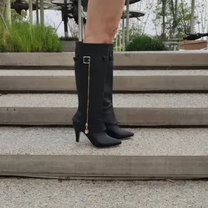 Vue latérale de bottes noires pointues à talons hauts avec fermeture éclair dorée.