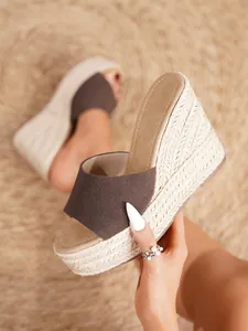 Detalle de sandalias con cuña para mujer con suelas trenzadas de paja y tiras marrones.