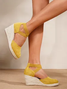 Detalle de sandalias amarillas con cuña de esparto y correas elásticas al tobillo