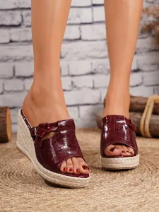 Detail of burgundy crocodile embossed wedge espadrilles on a woven mat