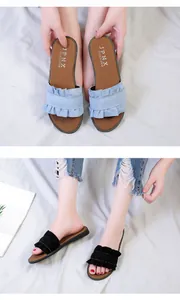 Close-up of stylish women's flat slides with ruffled edges and denim fabric detail.