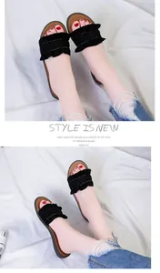 Close-up detail of black ruffled edge slide sandals worn with distressed jeans.