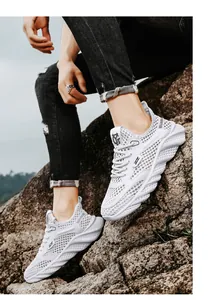 Close-up detail of men's white breathable hollow-out mesh running shoes on natural rocks