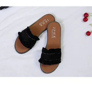 Detailed view of women's flat sandals featuring black ruffled straps and tan soles