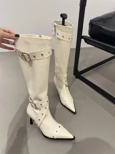 Detailed view of cream studded knee-high boots with pointed toe and stiletto heel.