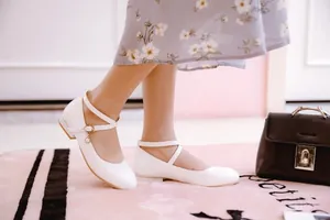 Close-up of elegant white patent leather Mary Jane flats featuring a delicate pearl charm
