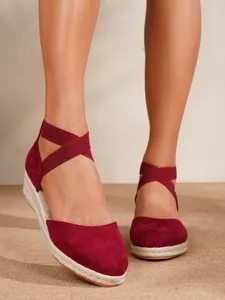 Primer plano de sandalias de esparto con cuña en ante burdeos y correas elásticas