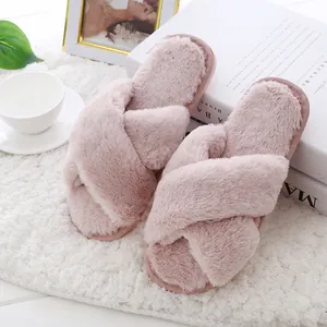 Detail view of soft pink faux fur slippers with criss-cross straps on a white rug.