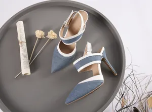 Detalle de sandalias de tacón de aguja en denim azul con correas blancas y punta.
