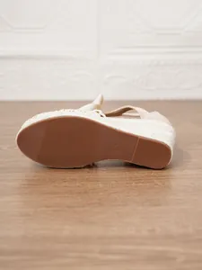 Detalle de sandalias de cuña en lona beige que muestra la suela de goma texturizada