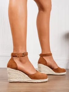 Detailed shot of brown suede wedge sandals featuring straw woven soles and ankle straps