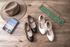 Detail of black and white Mary Jane shoes with double ankle straps on wooden surface.