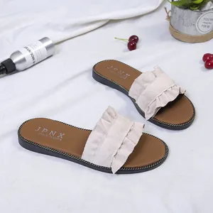 Macro view of textured beige ruffle strap and golden chain detail on summer flat slippers