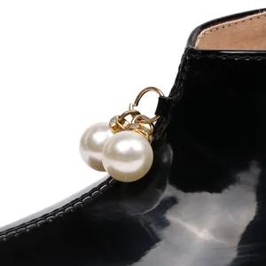 Close-up of pearl bead charms on black patent leather shoes with gold hardware.