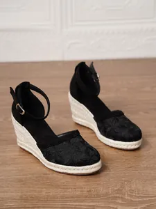 Detalle de sandalias de cuña negras con bordado de encaje floral y correa en el tobillo.