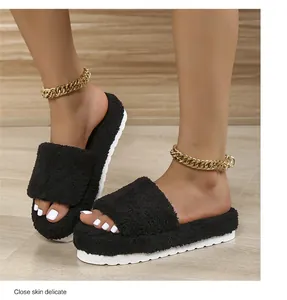 Detailed view of black fuzzy platform slide slippers worn with gold chain anklets