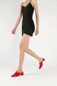 Mules rouges vernies à talons épais portées avec une mini-robe noire scintillante