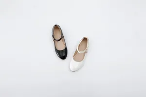 Detail view showing black and white glossy Mary Jane shoes with adjustable buckle straps