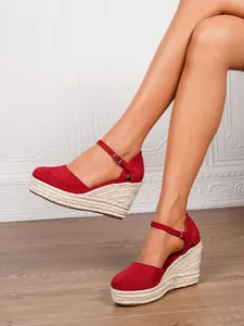 Rote Espadrilles-Sandalen mit Keilabsatz, geschlossener Kappe und Knöchelriemen am Fuß.