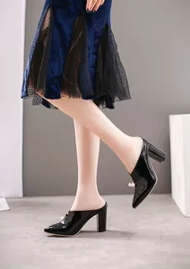 Detail shot of black patent leather pointed-toe block-heel mules with pearl beads.