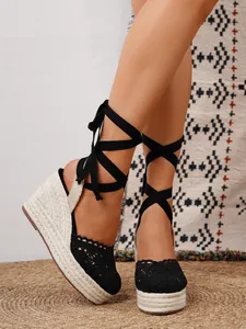 Primer plano de elegantes sandalias alpargatas de cuña negras con cordones y ganchillo