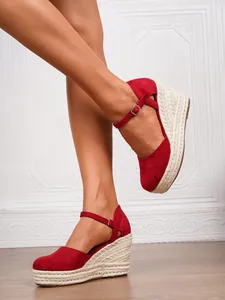 Rote geschlossene Espadrille-Keilsandalen mit Knöchelriemen an einem Modell.
