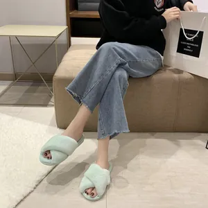 Detail view of mint green cross-strap fuzzy slippers worn by a model in a cozy home setting