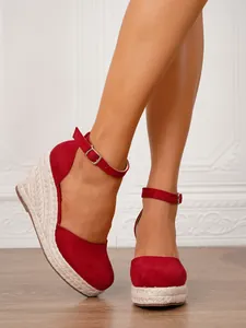 Primer plano de sandalias de cuña en ante rojo con plataforma de esparto y correa al tobillo