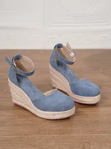 Vista de detalle de sandalias de cuña de esparto de ante azul con correas al tobillo.