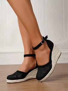 Primer plano de elegantes sandalias de esparto con cuña en encaje floral negro y yute