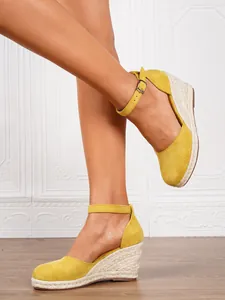 Detailed side view of yellow suede espadrille wedge sandals with ankle straps on model