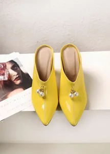 Detail view of vibrant yellow pointed-toe mules featuring elegant pearl bead charms.
