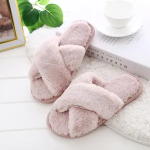 Close-up detail of soft pink fuzzy cross-strap indoor slippers on a white table
