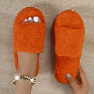 Vibrant orange fuzzy slippers with plush faux fur and platform sole on wood floor.