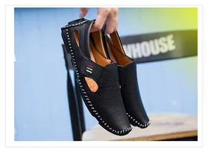 Close-up of hand holding black leather men's loafers with white contrast stitching.
