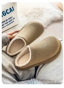 Close-up view of tan suede slippers featuring soft white plush lining and thick comfortable soles.