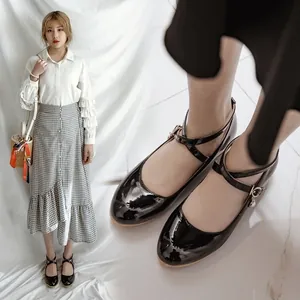 Close-up of glossy black Mary Jane flat shoes with cross straps and pearl charms.
