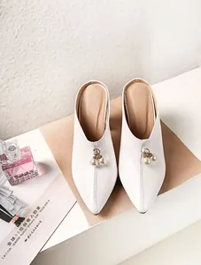Macro detail of elegant white pointed-toe mules featuring pearl charms and fine stitching.