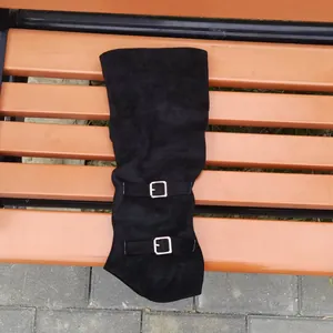 Detail view of black suede over-the-knee boots with stylish silver buckles on a bench.