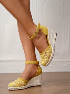 Sandalias de cuña con encaje floral amarillo usadas por una modelo en un ambiente interior.