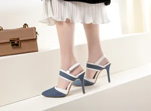 Primer plano de sandalias de tacón de aguja en denim azul y cuero blanco en una modelo