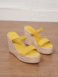 Vista detallada de sandalias de cuña en ante amarillo con plataforma de cuerda tejida.